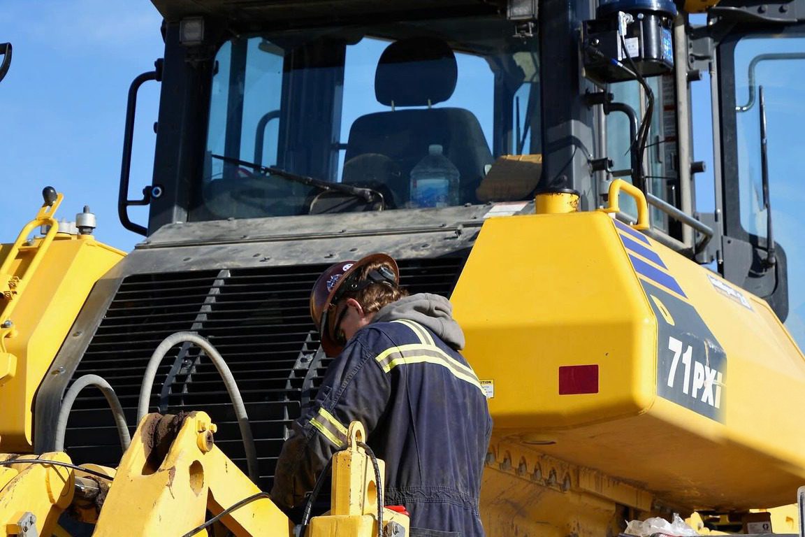 Caden Cope working on the front linkage of a yellow Komatsu dozer